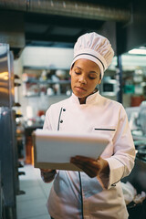 Wall Mural - African American female chef taking notes while working in restaurant.