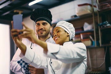 Wall Mural - Happy cooks taking selfie while working at restaurant kitchen.