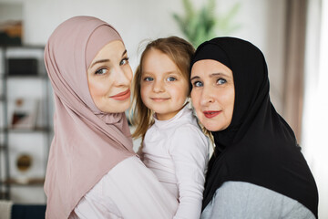 Wall Mural - Muslim grandmother, daughter and grandchild together at home, happy domestic life moments. Family having fun, concepts about elderly, mult-generation islamic family and relationship