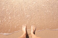 Woman's Feet Standing On Sandy Beach 