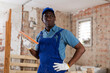 Portrait of professional african american plasterer wearing blue overalls and cap standing with sponge float in hands inside building under construction