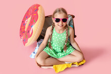 Cute Little Girl Sitting In Suitcase On Pink Background