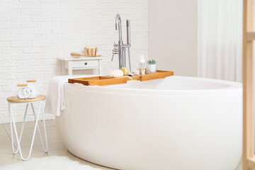 Poster - Modern bathtub with wooden tray and different supplies in bathroom interior