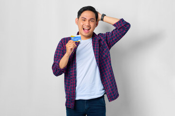 Wall Mural - Smiling young Asian man in plaid shirt showing credit card isolated on white background