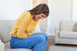 © Graphicroyalty - Woman lying on sofa looking sick in the living room. Beautiful young woman lying on bed and holding hands on her stomach. Woman having painful stomachache on bed, Menstrual period