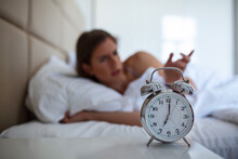 Woman Lying In Bed Turning Off An Alarm Clock In The Morning At 5am. Hand Turns Off The Alarm Clock Waking Up At Morning, Girl Turns Off The Alarm Clock Waking Up In The Morning From A Call.