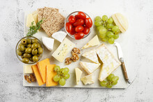 Cheese Platter With Organic Cheeses - Blue Cheese Cheddar, Emmantaler, French Soft Cheese With Strong Smell, Italian Parmesan, Grapes, Tomatoes, Olives, Nuts And Crackers On Marble Board