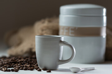 Canvas Print - Shallow focus of a cup of hot coffee with coffee beans and white container in the background