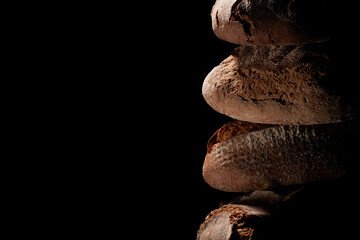 Canvas Print - Closeup of fresh-baked loaves stacked on top of each other against a black background