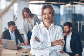 Wall Mural - Portrait of beautiful smiling mature businesswoman with her colleagues on background in office.