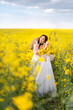 © Марина Шавловская - young beautiful woman is sitting in a field with yellow flowers. A girl in a long white dress enjoys nature