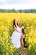 © Марина Шавловская - woman in a long white dress and black boots is sitting in a rapeseed field . The girl enjoys nature and freedom