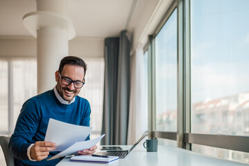 Wall Mural - happy business professional analyzing documents while sitting at office desk