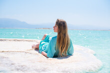 Young Woman In Turquoise Flying Pelerine Lies On White Salt Island Dead Sea And Gets Enjoy. Travel And Vacation In Summer In Israel