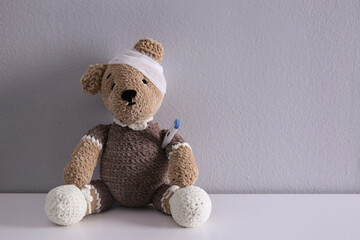 Canvas Print - Cute toy bear with bandage and thermometer on white table, space for text. Children's hospital