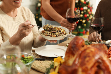 Poster - Woman with bowl of traditional Christmas kutia and her family at festive dinner, closeup. Slavic dish