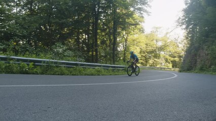 Wall Mural - Caucasian male racing cyclist riding uphill on an open roads cycling route, handheld wide shot.