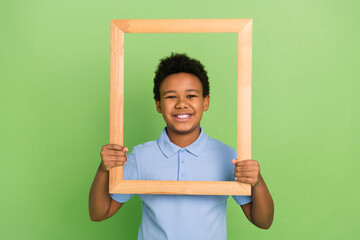 Wall Mural - Portrait of handsome cheerful pre-teen boy holding photo frame posing hobby isolated over green color background