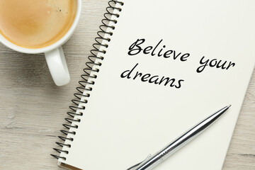 Wall Mural - Motivational quote Believe Your Dreams written in notebook on wooden table, flat lay