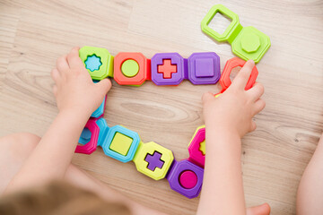 Colorful domino shapes game. Childs hand on part, connecting puzzle pieces. Montessori type educating toy. Fine motor skils. Kid Sense Child Development.
