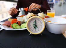 Close Up  Yellow Alarm Clock While Man Intermittent Fasting Concept With Eating Salad  Plates. Time To Lose Weight , Eating Control Or Time To Diet Concept