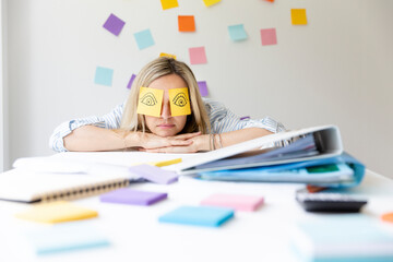 Wall Mural - Business woman sits behind her desk on which are many office things and has sticky notes with drawn eyes on her face and sleeps