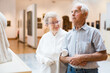© caftor - mature European couple examines paintings in an exhibition in hall of art museum