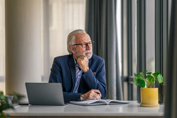 Thoughtful senior manager planning strategy while working on laptop at desk