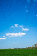 High metal electricity pylons with power lines that pass over an agricultural field, against the backdrop of a blue sky and clouds.