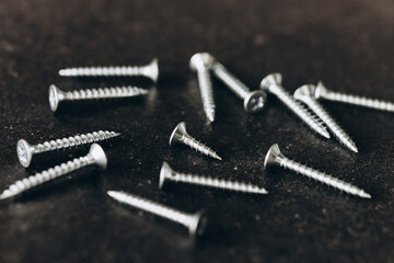 Poster - Metal tapping screws for wood on dark wooden background. Construction equipment concept. 