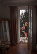 © NASTYA PALEHINA - teen leisure. young brunette girl in black dress sits casual near bouquets pink flowers and smiles cute on the french balcony in vintage interior background with mirror. lifestyle concept, free space