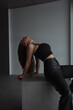 © NASTYA PALEHINA - closeup young brunette woman in black top and leather pants is sitting fashion in profile on the gray cube and looking up on the white wall background in loft interior. fashion concept, free space