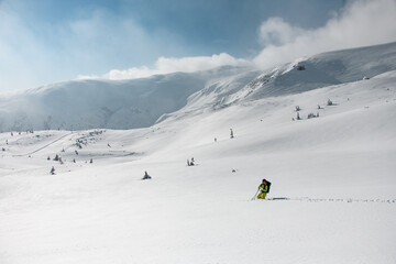 Smiling skier man in bright ski suit, helmet and googles standing standing in the snow knee-deep