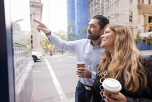 Couple With Coffee Looking At Map Board In City
