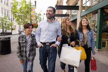 Happy Family With Shopping Bags Walking Arm In Arm In City