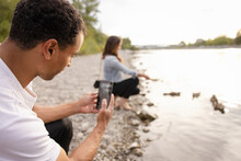 Man Photographing Girlfriend Feeding Ducks At Riverbank