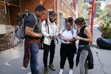 Woman Helping Young Backpacker Friends With Map On Urban Sidewalk