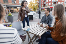Woman Greeting Friends Drinking Coffee At Urban Sidewalk Cafe