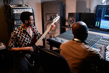 Stylish Young Black Musician Playing Electric Guitar While Music Producer Working On Mixing Console In Recording Studio