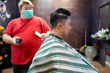 Wall Mural - Client sitting while a fat barber is cutting her hair with an electric razor