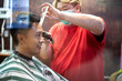 Fat barber with facial mask cutting the hair of an asian client in a barber shop