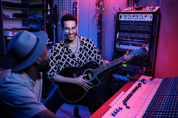 Wall Mural - Professional producer and young African American guitar player having fun while working on album in recording studio, neon lighting