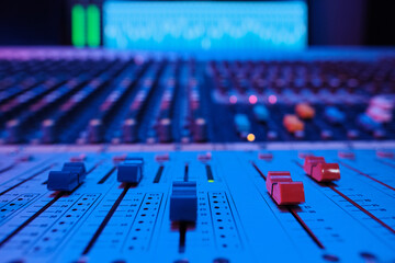 Wall Mural - Close-up shot of mixing console buttons and sliders in blue neon light in modern recording studio