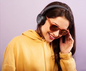 Canvas Print - Fun enjoying pretty young woman listen the music with long brow hair looking down in fashion yellow sport hoodie and sun glasses on purple background. Happy closeup