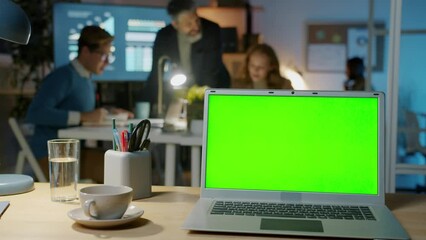 Laptop with chroma key green screen and business people diverse team working in dark office at night. Modern technology and workplace concept.