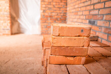 Red Bricks Stacked At A Construction Site, Close-up. The Bare Brick Walls Of An Unworthy House. The Doorway Is Closed With Polythene Film