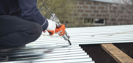 Worker using glue gun with adhesive to fix the metal steel on the roof.