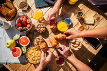Vertical View Of Table Full Of Breakfast Food And Group Of People Eating And Enjoying It Using Mobile Phone. Family And Friends Eat Together And Enjoy Morning Leisure Time. Bakery And Fruit