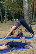 © irissca - Family fitness and yoga. Happy mom exercising with baby girls on grassy land against trees in forest. Young woman doing yoga exercise outdoors with her daughters together