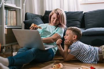 Canvas Print - single mother and son enjoying time together at home, using laptop computer and eating pizza